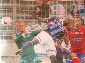 Pär Hansson blundar. Jörgen Mårtensson blundar, till och med Antom Webe blundar. Den ende som förmår hålla ögonen öppna är målskytten, den ende som verkligen rör bollen - Djurgårdens Mushekwi. Fotot är en detalj av ett TT-foto publicerat i Sportbladet 14/7-15. Förmodligen taget av Bildbyrån. 